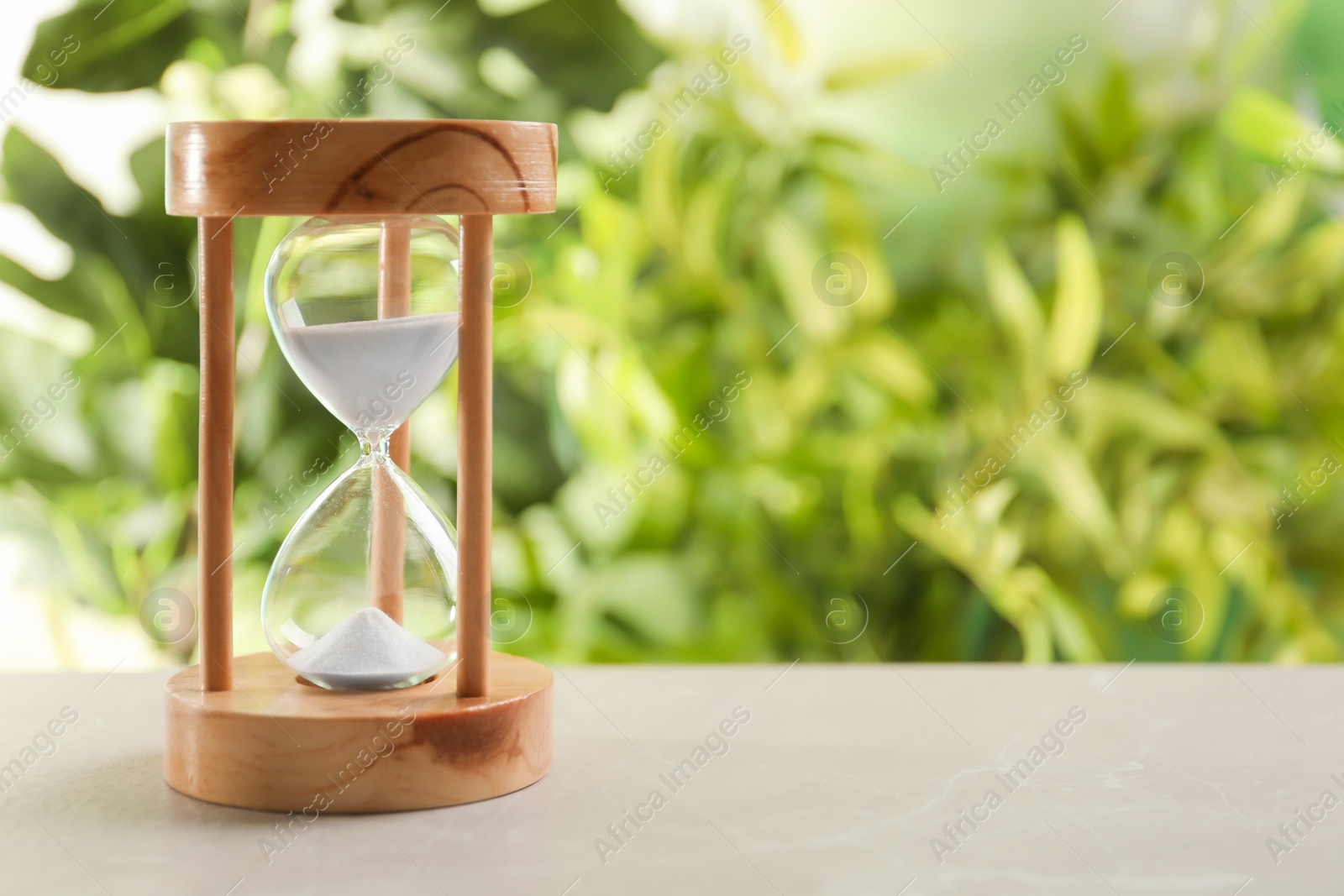 Photo of Hourglass with flowing sand on table against blurred background. Time management