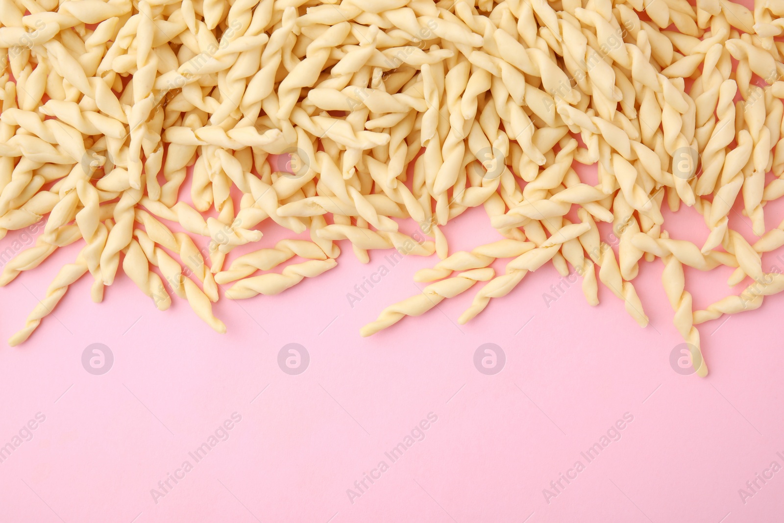 Photo of Uncooked trofie pasta on pink background, flat lay. Space for text