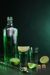 Photo of Absinthe in shot glasses, spoon, brown sugar cubes and lime on gray textured table. Alcoholic drink