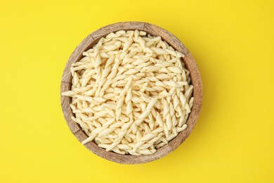 Photo of Uncooked trofie pasta in bowl on yellow background, top view