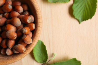 Photo of Tasty hazelnuts and green leaves on wooden table, top view. Space for text