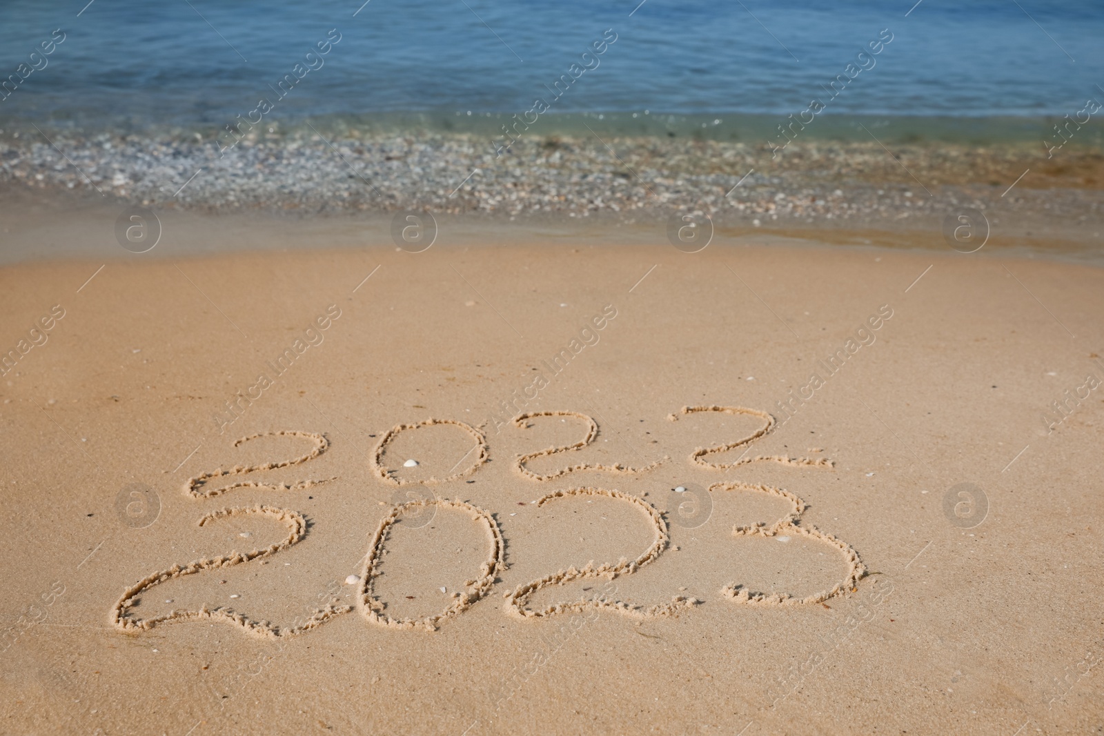 Photo of 2022 and 2023 written on sand at beach. New Year celebration