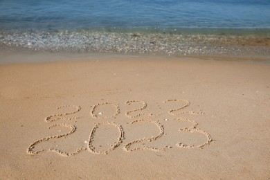 Photo of 2022 and 2023 written on sand at beach. New Year celebration