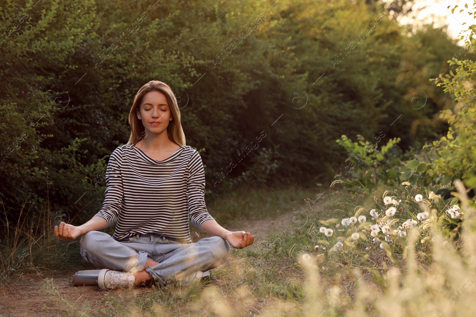 Photo of Young woman meditating on green grass outdoors, space for text