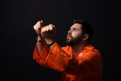 Photo of Prisoner in jumpsuit with handcuffs praying on black background
