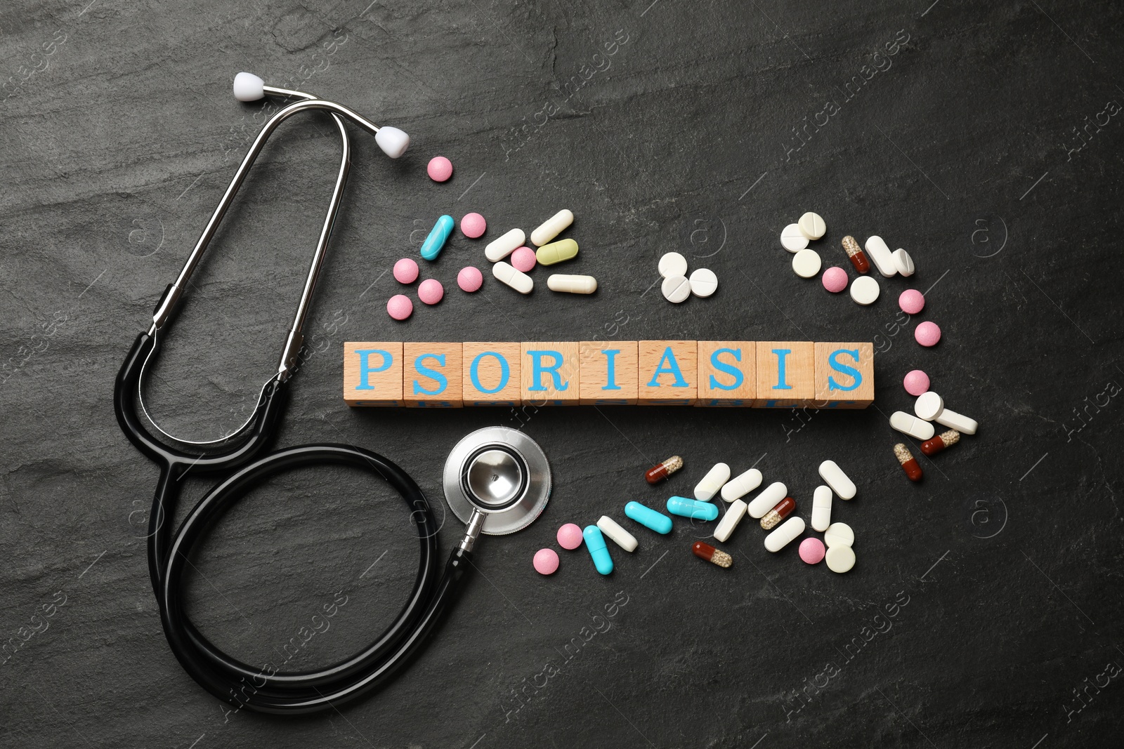 Photo of Word Psoriasis made of wooden cubes with letters, stethoscope and pills on dark gray textured table, flat lay