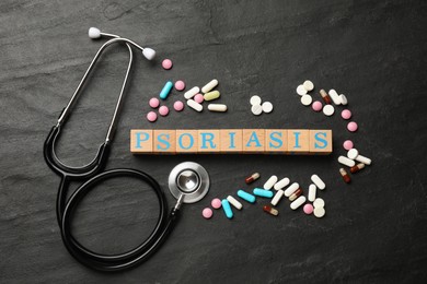 Photo of Word Psoriasis made of wooden cubes with letters, stethoscope and pills on dark gray textured table, flat lay