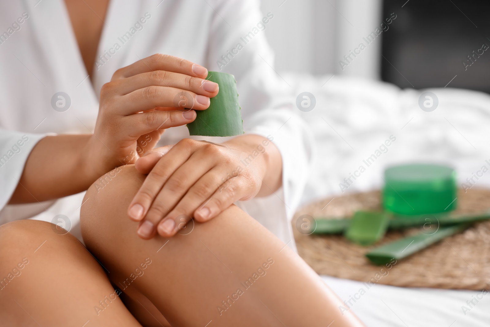 Photo of Young woman applying aloe gel from leaf onto her hand on bed, closeup. Space for text