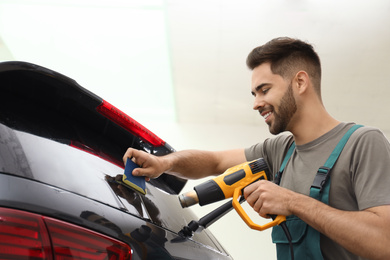 Worker tinting car window with heat gun in workshop