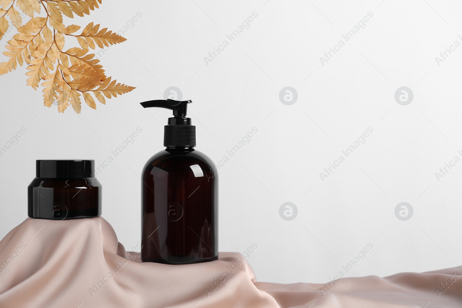 Photo of Different cosmetic product and dry leaves on pink fabric. Space for text