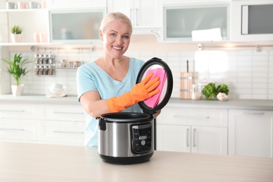 Mature woman cleaning modern multi cooker at table in kitchen