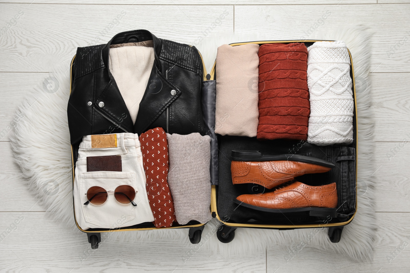 Photo of Open suitcase with folded clothes, shoes and accessories on floor, top view