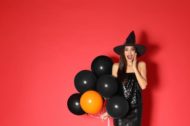 Photo of Beautiful young woman wearing witch costume with balloons for Halloween party on red background, space for text