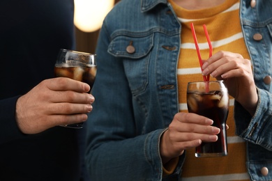 People holding glasses of cola with ice on blurred background, closeup