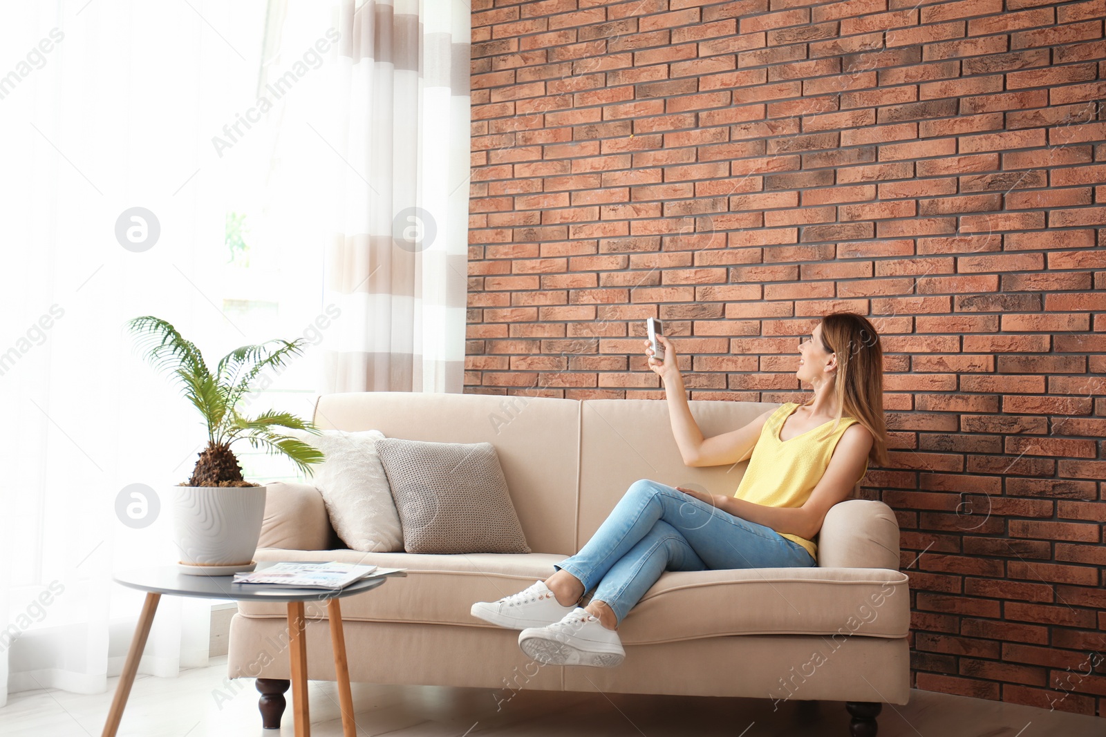 Photo of Woman with air conditioner remote at home