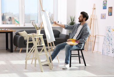 Photo of Man painting in studio. Using easel to hold canvas