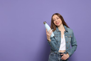 Beautiful young woman with thermos bottle on purple background, space for text