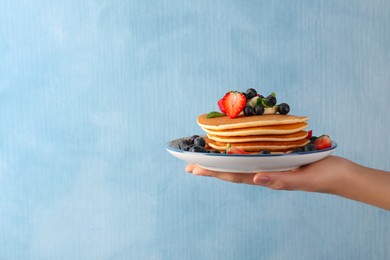 Photo of Woman holding delicious pancakes with fresh berries and butter against light blue background, closeup. Space for text
