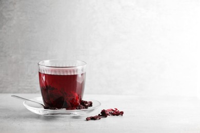 Photo of Aromatic hibiscus tea in glass, dried roselle calyces and spoon on light table, space for text