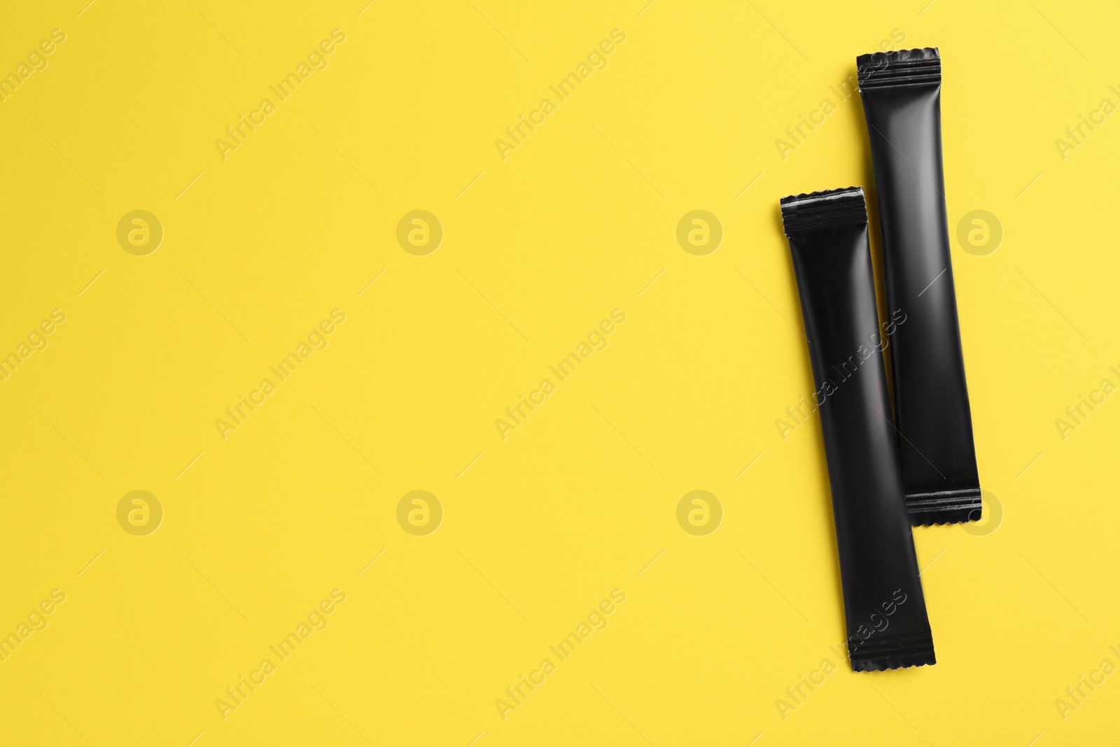 Photo of Black sticks of sugar on yellow background, flat lay. Space for text