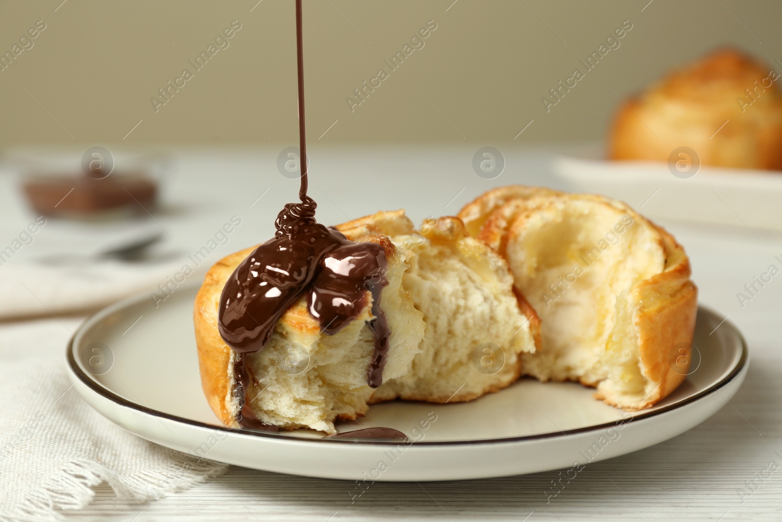 Photo of Pouring chocolate sauce onto delicious bun on white wooden table