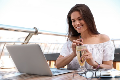Beautiful woman with refreshing drink and laptop at outdoor cafe
