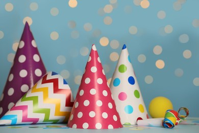 Photo of Colorful party hats and festive items on table against blue background with blurred lights