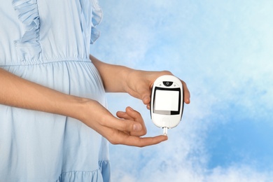 Pregnant woman checking blood sugar level with glucometer on color background. Diabetes test