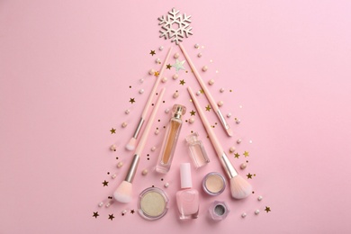 Photo of Christmas tree shape of decorative cosmetic products on pink background, flat lay\. Winter care