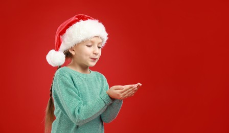 Happy little child in Santa hat on red background. Christmas celebration