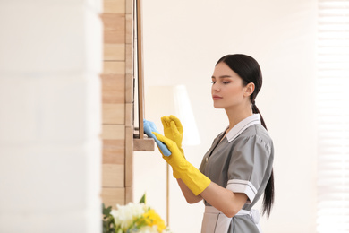 Photo of Young chambermaid wiping dust from furniture in hotel room