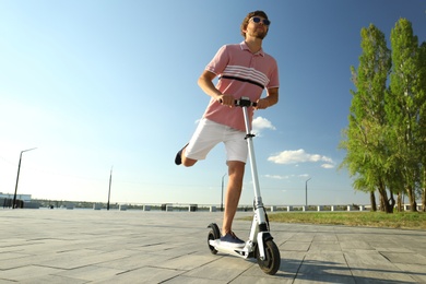 Man riding kick scooter along city street on sunny day