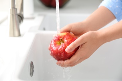 Woman washing fresh red apple in kitchen sink, closeup