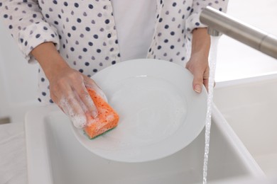 Photo of Woman washing plate above sink in modern kitchen, closeup