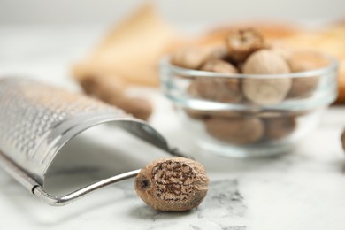 Nutmeg seeds and grater on white marble table, closeup