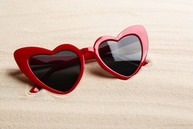 Stylish heart shaped sunglasses on white sand. Summer time