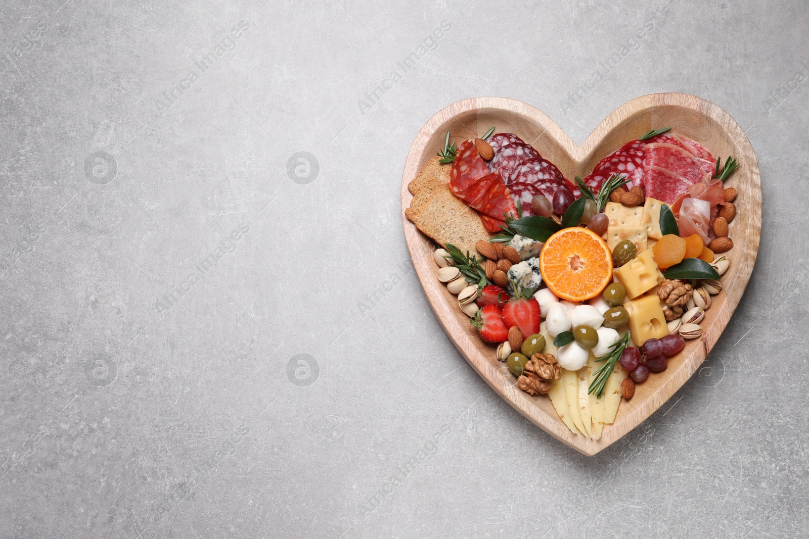 Photo of Heart shaped plate with different delicious snacks on grey table, top view. Space for text