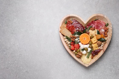 Heart shaped plate with different delicious snacks on grey table, top view. Space for text