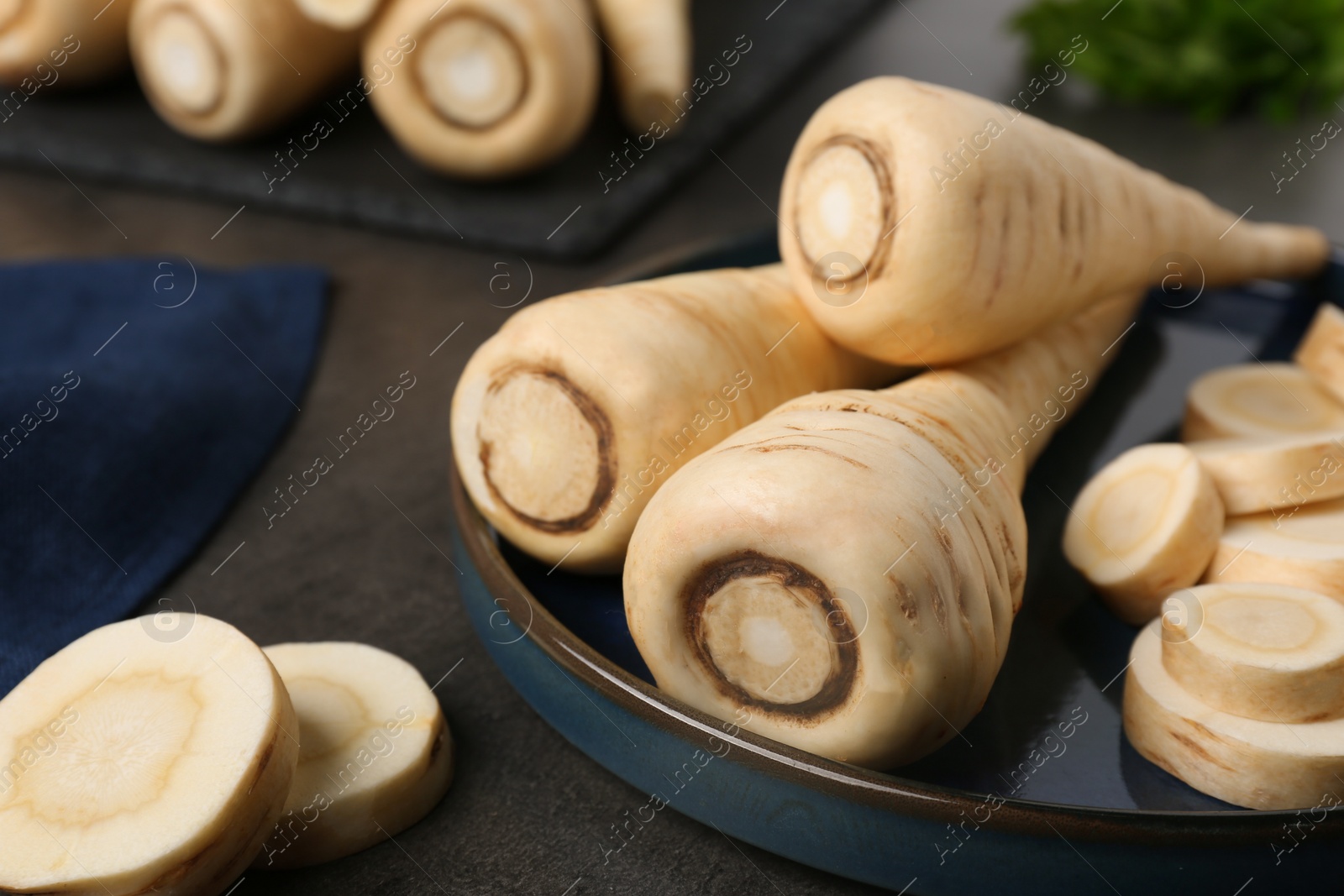 Photo of Whole and cut parsnips on black table, closeup