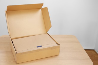 Photo of Open cardboard box with item wrapped in kraft paper on wooden table, space for text. Delivery service