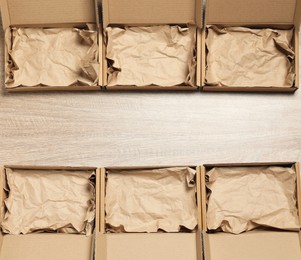 Photo of Many open cardboard boxes with crumpled paper on wooden background, flat lay. Space for text