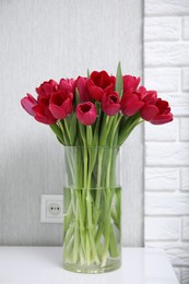 Photo of Bouquet of beautiful tulips in glass vase on white table indoors