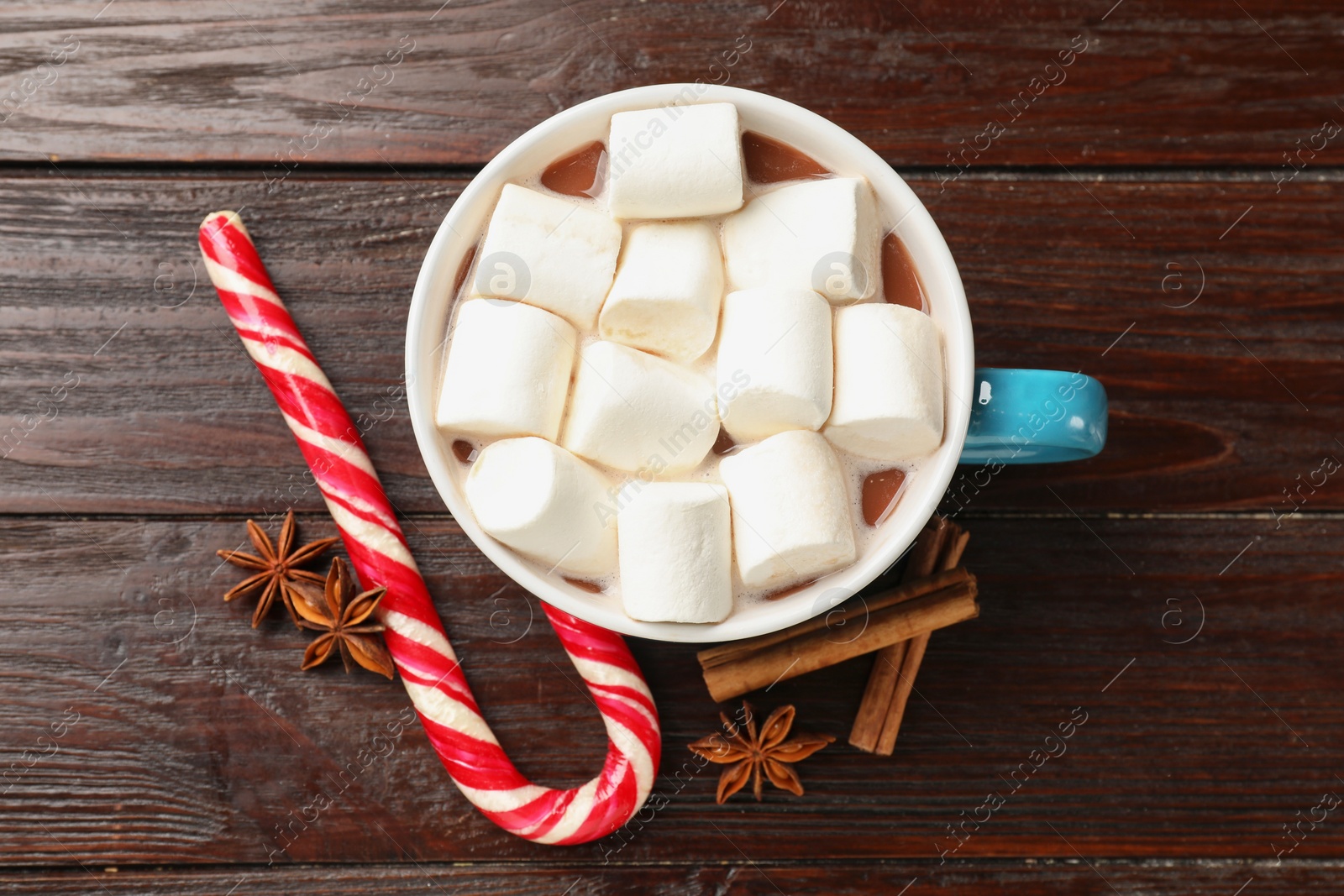 Photo of Tasty hot chocolate with marshmallows, candy cane and spices on wooden table, flat lay