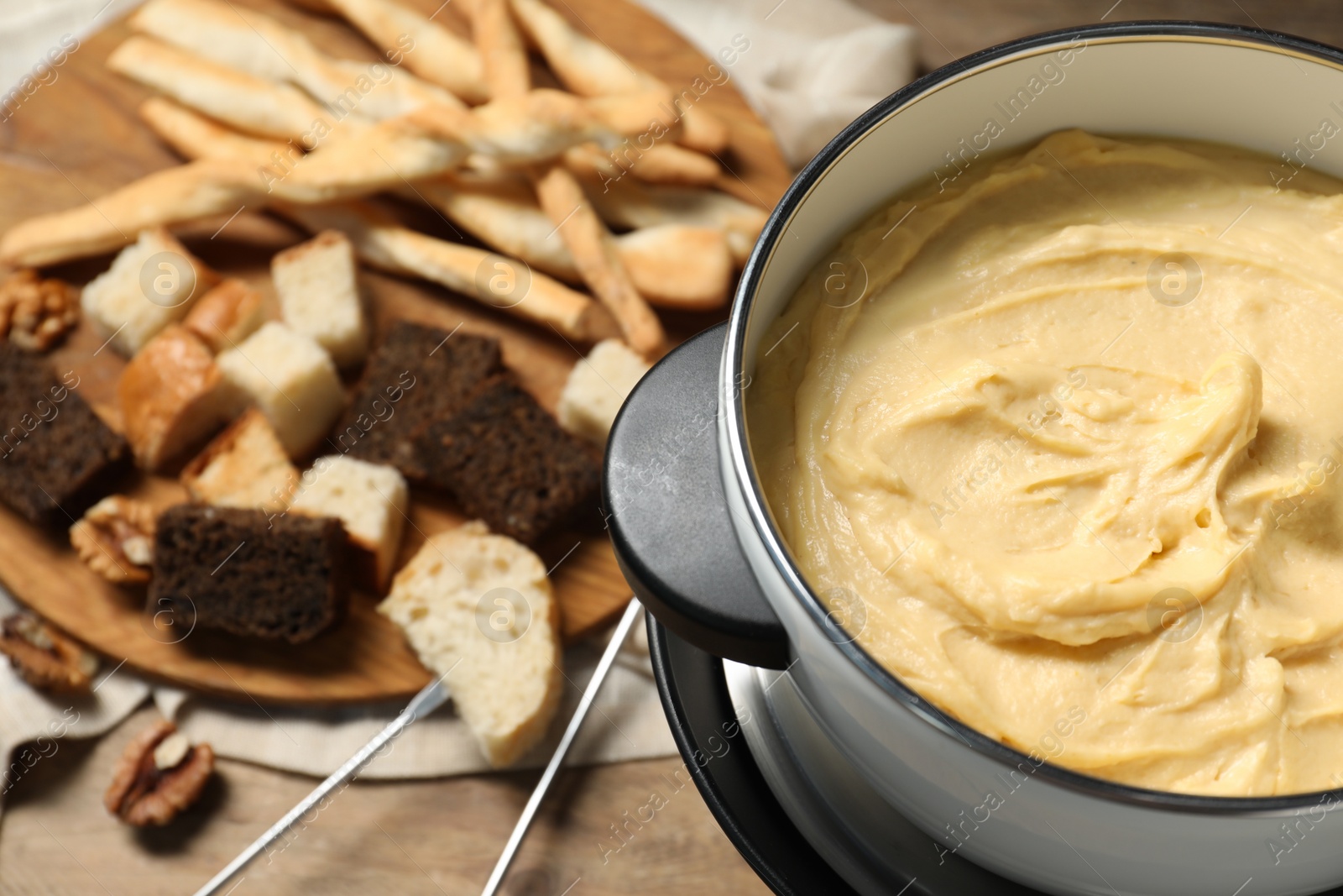 Photo of Tasty melted cheese in fondue pot and snacks on table, closeup