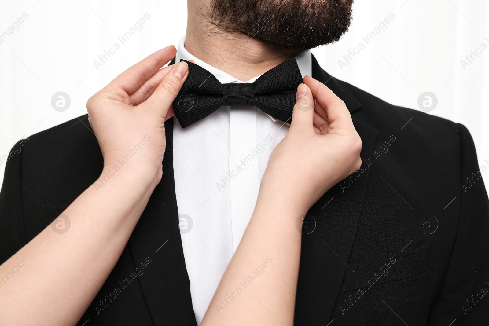 Photo of Woman adjusting bow tie to man indoors, closeup