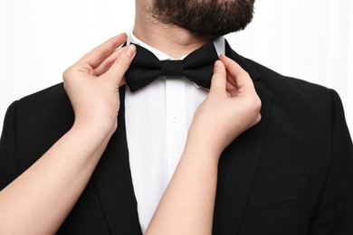 Photo of Woman adjusting bow tie to man indoors, closeup