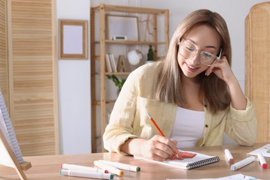 Photo of Young woman drawing in sketchbook with pencil at wooden table indoors