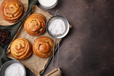 Photo of Sweet buns. Delicious rolls with raisins and powdered sugar on brown textured table, flat lay. Space for text