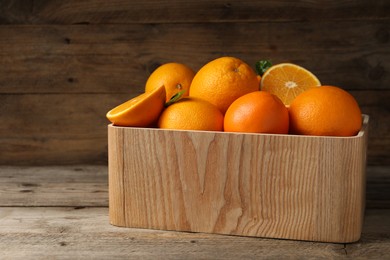 Many whole and cut ripe oranges on wooden table