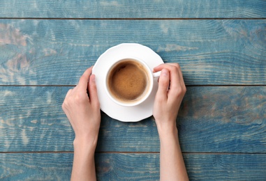 Young woman with cup of delicious hot coffee on wooden background, top view